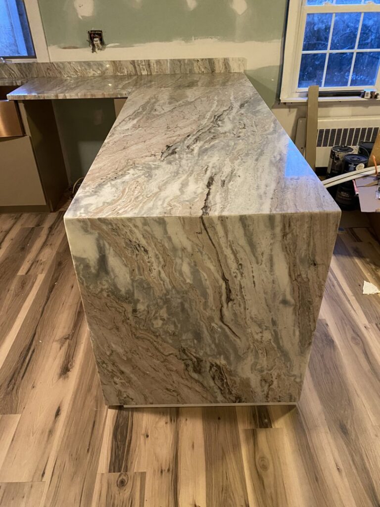 A custom marble or granite kitchen island with a waterfall edge, expertly installed by Fine Design Marble And Granite in Springfield, MA.