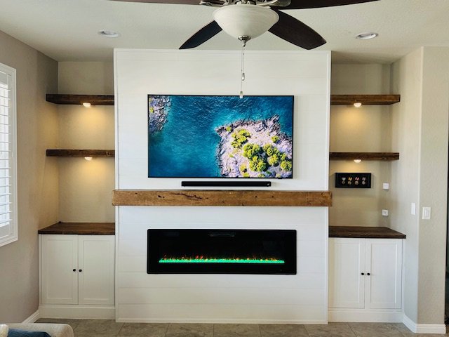 A custom-built media center with a mounted TV, electric fireplace, and floating shelves by Henderson Handyman in Henderson, NV