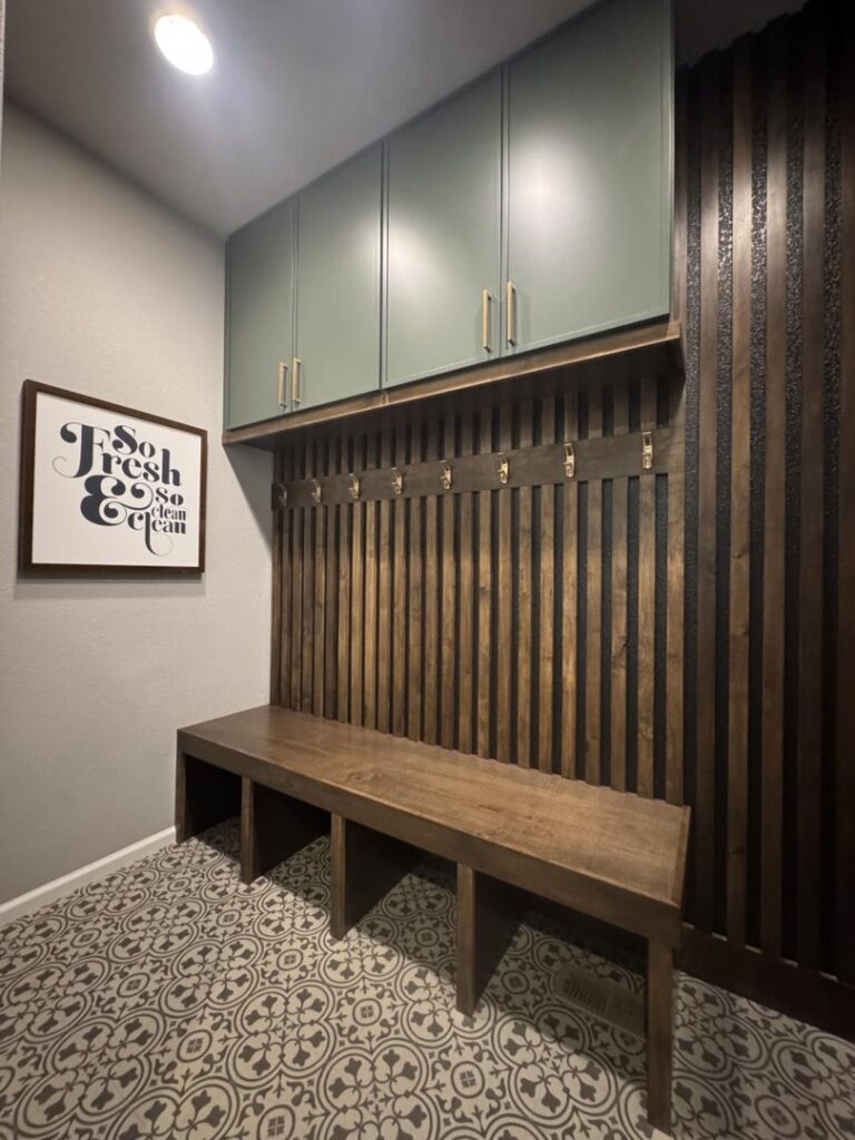 A custom mudroom featuring a wooden slatted wall, bench, and green upper cabinets by Colorado ProBuilt in Aurora, CO