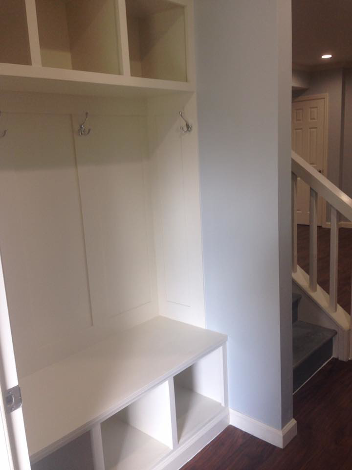 A custom-built white mudroom bench and storage unit with coat hooks by J Development in Pittsburgh, PA.