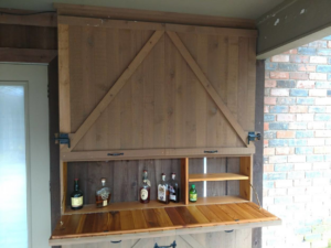 A custom outdoor bar cabinet with a fold-down counter and shelves, built by Rex Austin's Remodeling in Ball, LA.
