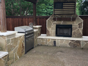 A custom outdoor kitchen with a stone fireplace and built-in grill by Tin Star Fencing in Fort Worth, TX