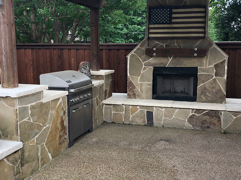 A custom outdoor kitchen with a stone fireplace and built-in grill by Tin Star Fencing in Fort Worth, TX