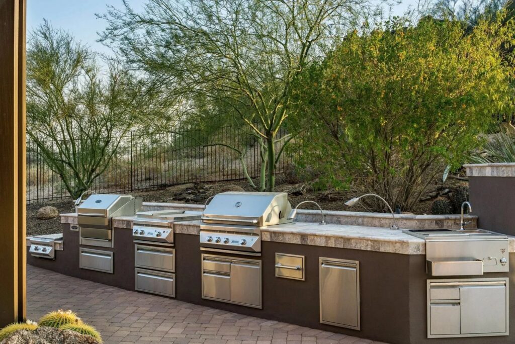 A custom outdoor kitchen with multiple grills and sinks installed by Envy Pools in Gilbert, AZ.