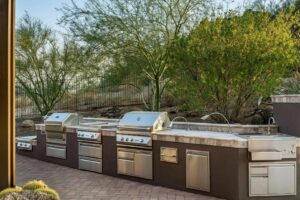 A custom outdoor kitchen with multiple grills and sinks installed by Envy Pools in Gilbert, AZ.