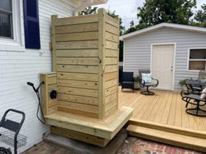 A custom-built outdoor wooden shower enclosure and connecting deck by Seaside Craftworks LLC in Wilmington, NC.