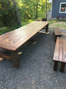 A custom-built long outdoor wooden table with matching benches on a gravel patio by Davidson Handyman Services in Nashville, TN.