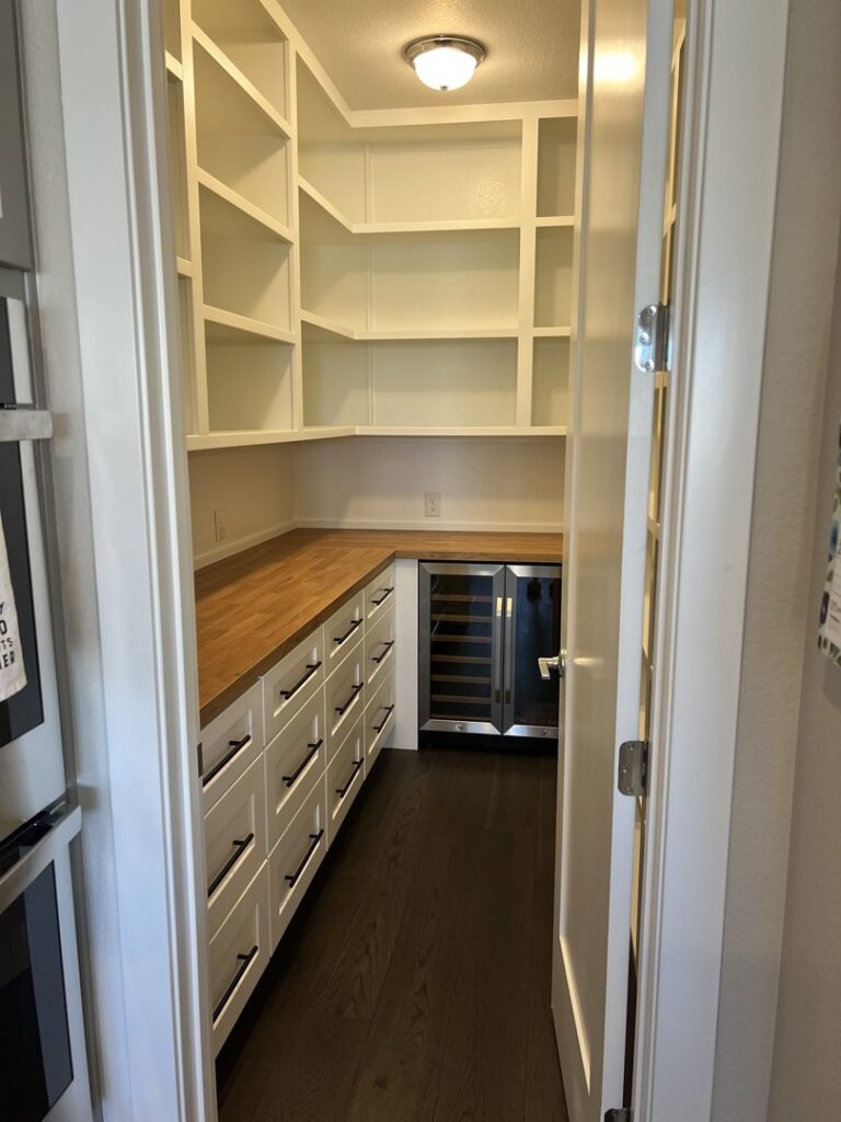 A custom-built pantry with white shelving, wooden countertops, and an integrated wine fridge by Colorado ProBuilt in Aurora, CO