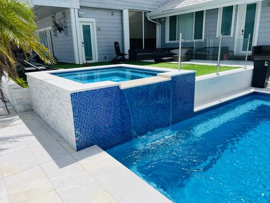 A custom pool with a raised spa and elegant waterfall feature, expertly installed by BAFCO POOLS in Hialeah, FL.