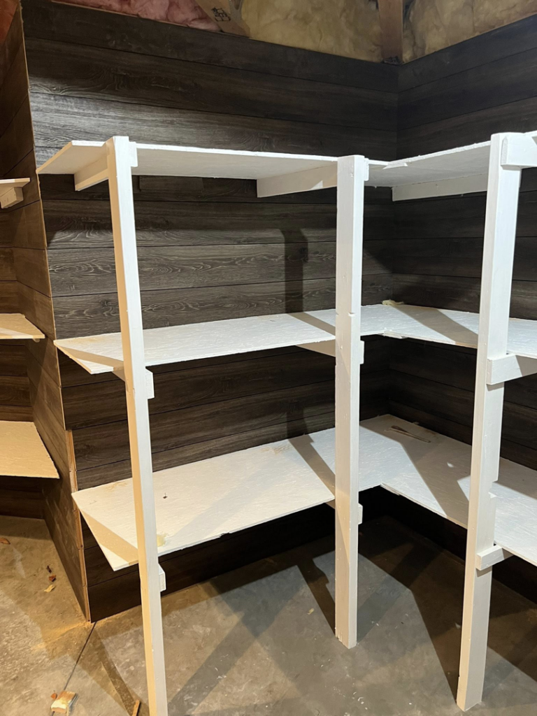 Multiple custom white shelving units installed against a dark wood-paneled wall by Halls Home Solutions in Pierre, SD