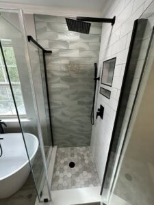 A custom shower installation featuring unique wavy wall tiles, hexagonal floor tiles, and black fixtures by MPH Design in Philadelphia, PA.