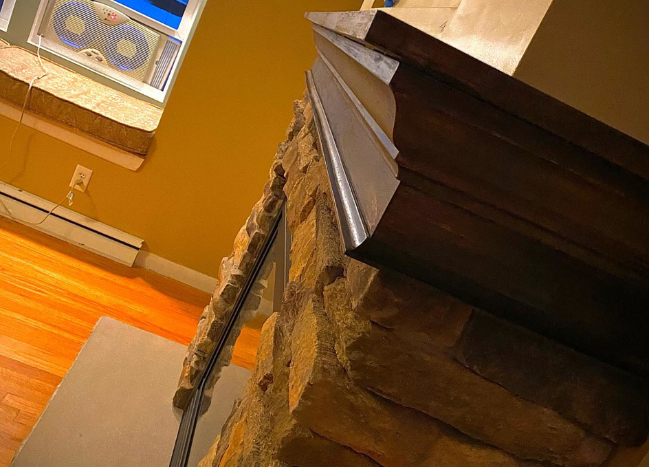 A close-up view of a custom stone fireplace with a dark wooden mantel by Mohawk Home Improvement of Syracuse LLC in Syracuse, NY.