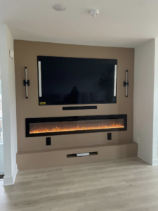 Custom-built media wall with mounted TV, electric fireplace, and shelving by Wareham Home Improvements in Frederick, MD.