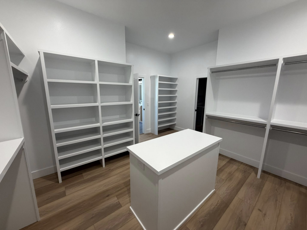 Custom white built-in shelving and an island in a walk-in closet by ELS Construction in Springfield, MO.