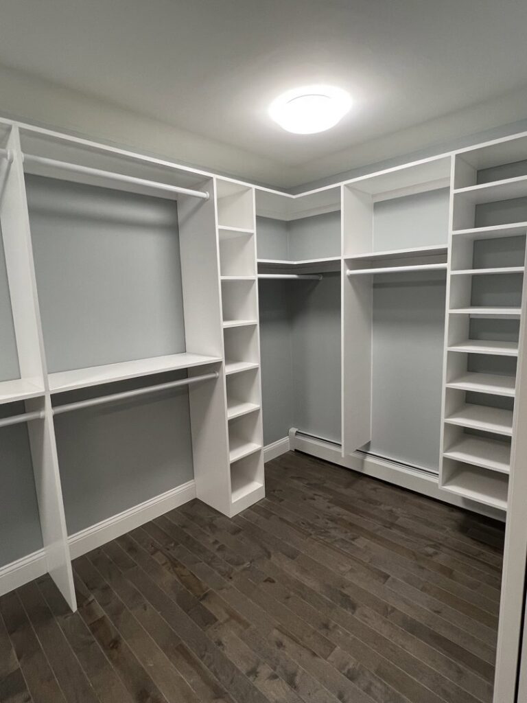 Custom white shelving and hanging rods installed in an empty walk-in closet by CWS Handyman LLC in Seekonk, MA