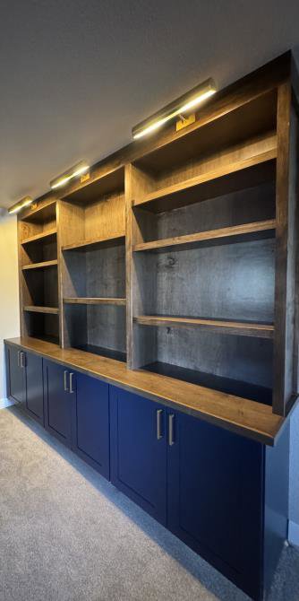 A custom dark wood built-in bookshelf and blue lower cabinets with accent lighting by Colorado ProBuilt in Aurora, CO