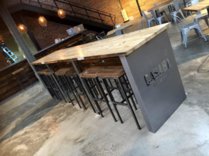 A custom-built long wooden table with a metal base and stools installed by Recreated in Birmingham, AL.