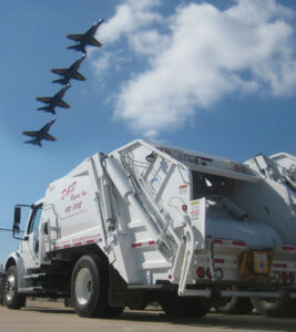 The rear view of a D&D Refuse Inc. garbage truck with fighter jets flying in formation overhead in Lincoln, NE.