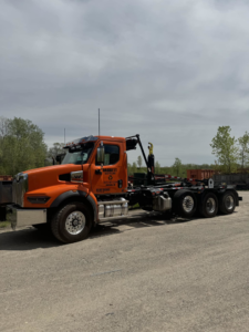 An orange roll-off truck from Daggett Container Service LLC, used for container delivery in Lansing, MI.