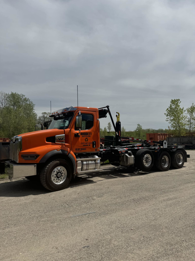 An orange roll-off truck from Daggett Container Service LLC, used for container delivery in Lansing, MI.