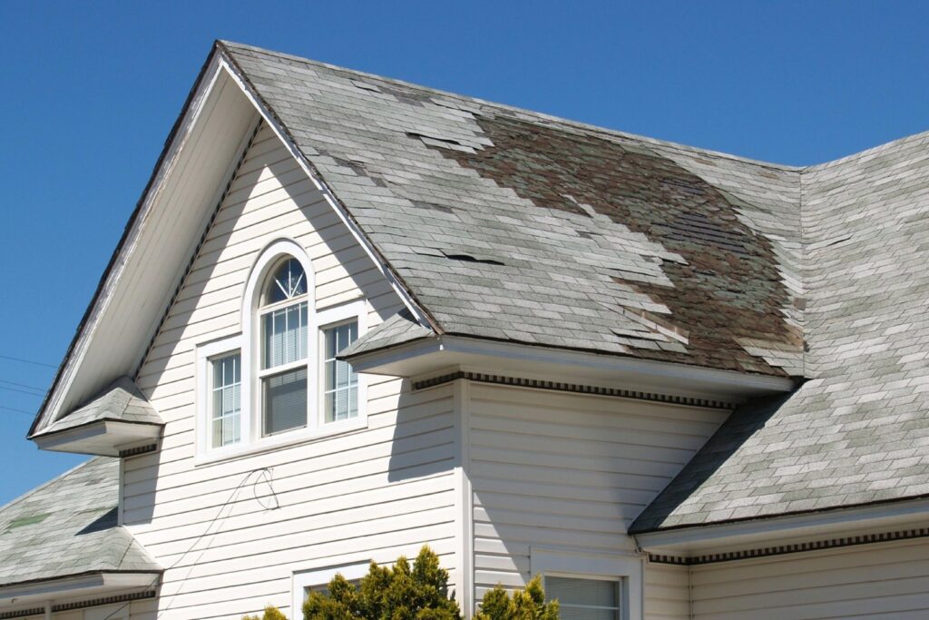 A residential house with a severely damaged and peeling asphalt shingle roof, indicating a need for repair by Prescott Roofing and Masonry in Carnegie, PA.