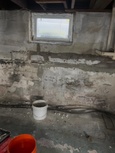 Damaged basement wall with cracks and peeling paint, ready for handyman repair by Calnan Site Development LLC in Lynn, MA.