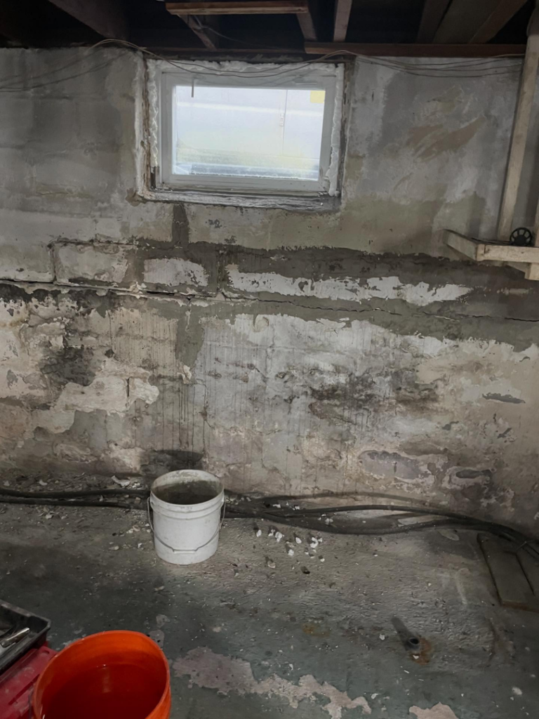 Damaged basement wall with cracks and peeling paint, ready for handyman repair by Calnan Site Development LLC in Lynn, MA.