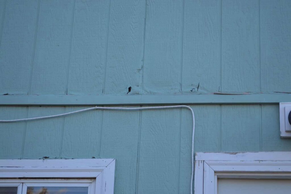 Close-up of damaged exterior siding on a house, indicating a need for repair by Knutson's Property Maintenance Llc in Williston, ND.