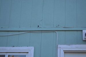 Close-up of damaged exterior siding on a house, indicating a need for repair by Knutson's Property Maintenance Llc in Williston, ND.