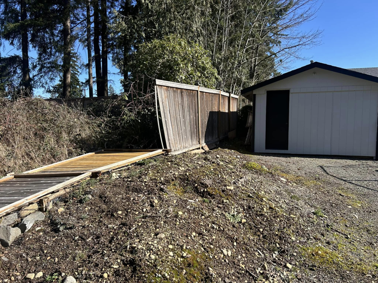 A damaged wooden fence section lying on the ground next to a shed, ready for repair by HandyMan Shocks in Tacoma, WA.