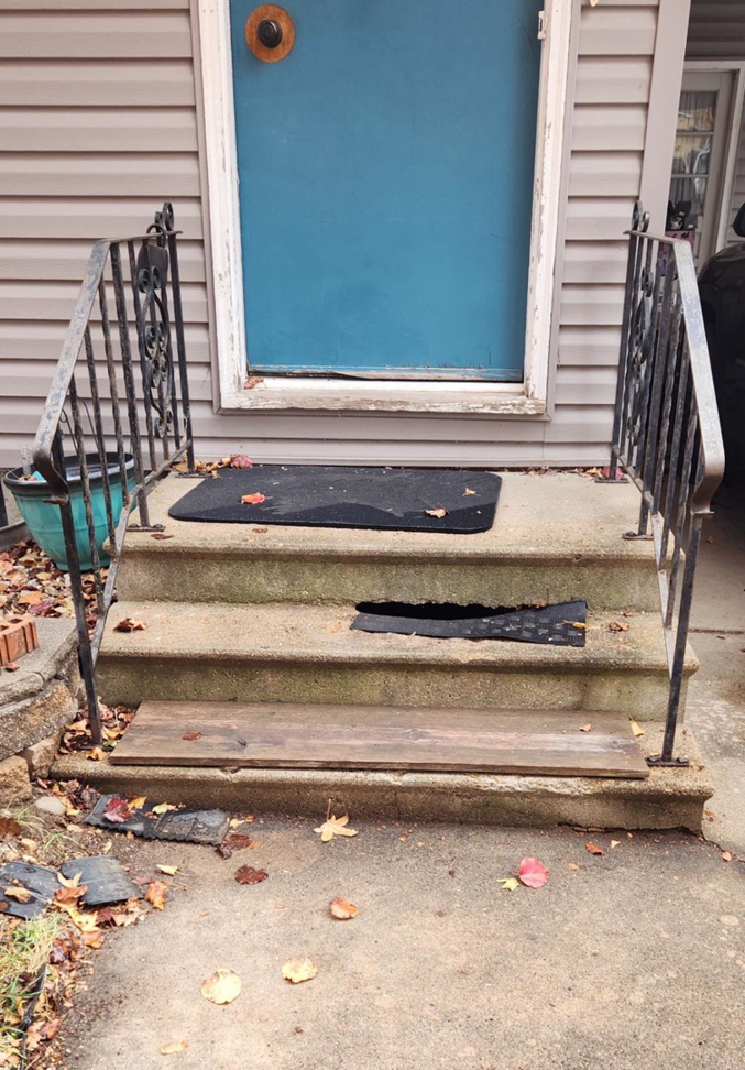 A damaged front porch with broken concrete steps and rusty railings needing repair by Bill's Handyman Services in Anchorage, AK.