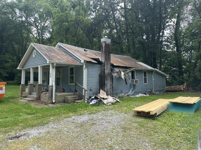 Four Seasons Roofing and Exteriors providing junk removal services for a damaged house with debris and a dumpster in Lakewood, CO.