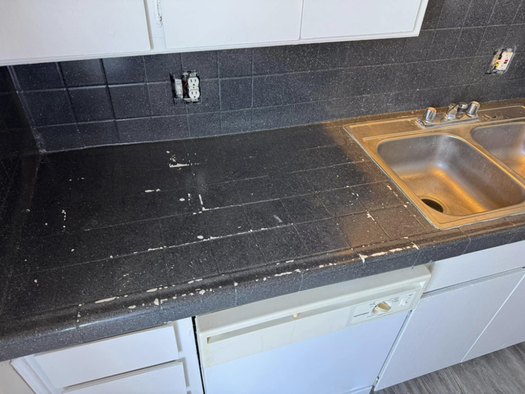 A damaged black tiled kitchen countertop showing wear and peeling, before resurfacing by That Resurfacing Guy LLC in Oklahoma City, OK.