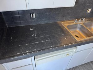 A damaged black tiled kitchen countertop showing wear and peeling, before resurfacing by That Resurfacing Guy LLC in Oklahoma City, OK.