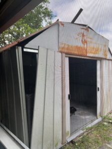 A damaged metal shed undergoing demolition, showing the type of removal service offered by Junk Fade Away, LLC in Jacksonville, FL.