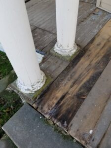 Damaged wooden porch floorboards and peeling paint on columns, ready for repair by Honey Bee's Handyman Services in Hastings, NE.