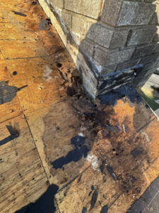 Damaged roof decking and flashing around a brick chimney, indicating a repair job by Conway's Roofing in Richmond, KY.