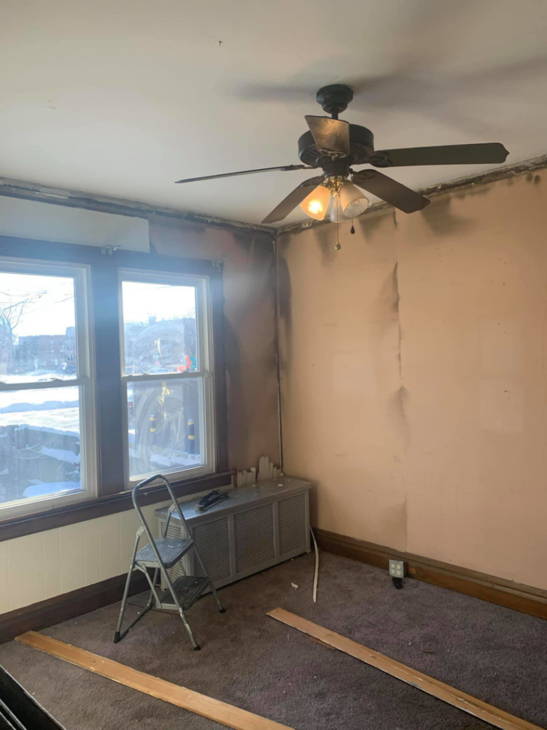 A damaged room before renovation, showing walls needing repair and an old ceiling fan, by UpGray'D Remodeling LLC in Chicago, IL.
