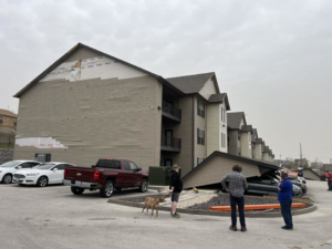 An apartment building with damaged siding and a collapsed carport, showing storm damage repair work by Larson Exteriors in Sunset Hills, MO.