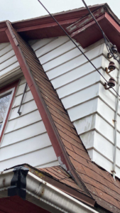 Close-up of damaged siding, worn roof shingles, and old gutters on a house, indicating needed repairs by The Roof Guy in Fort Lauderdale, FL.