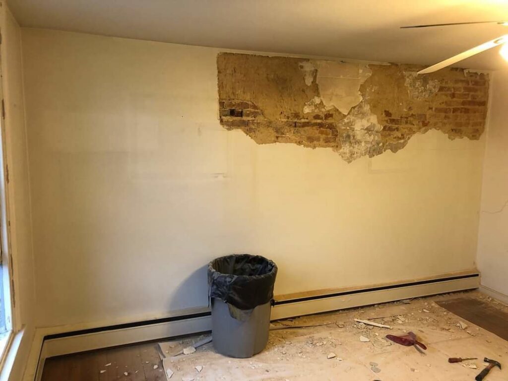 A damaged wall with exposed brick and crumbling plaster, indicating a repair project by N. Bennecoff Drywall & Plaster in Lancaster, PA.