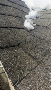 Close-up of wet asphalt roof shingles with melting snow, showing potential damage or wear that Crown Remodeling can repair in Owings Mills, MD.