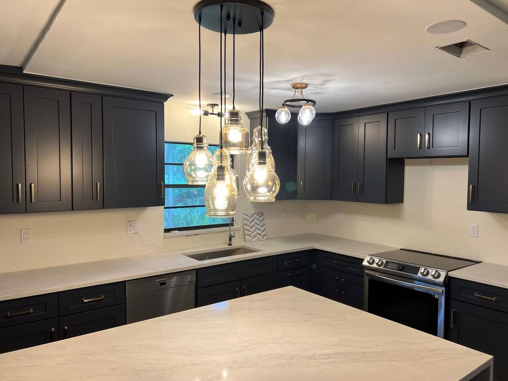 A stylish kitchen remodel featuring dark blue cabinets and modern pendant lighting by Beyond Builders in Tampa, FL