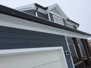 Dark gutters installed on a house during a light snowfall, maintained by Gutter Flow7 LLC in Madison, WI.