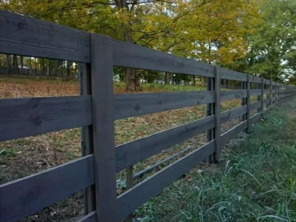 A long, dark-stained wooden post and rail fence, showcasing fence staining services by Steven's Deck and Fence Staining Columbus, GA.