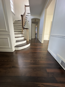 A stunning dark wood floor in an entryway with a grand staircase, completed by SANDMAN WOOD FLOOR REFINISHING in Cleveland, OH.