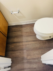 Freshly installed dark wood-look laminate flooring in a bathroom by NGU Contracting Solutions LLC in Albany, GA.