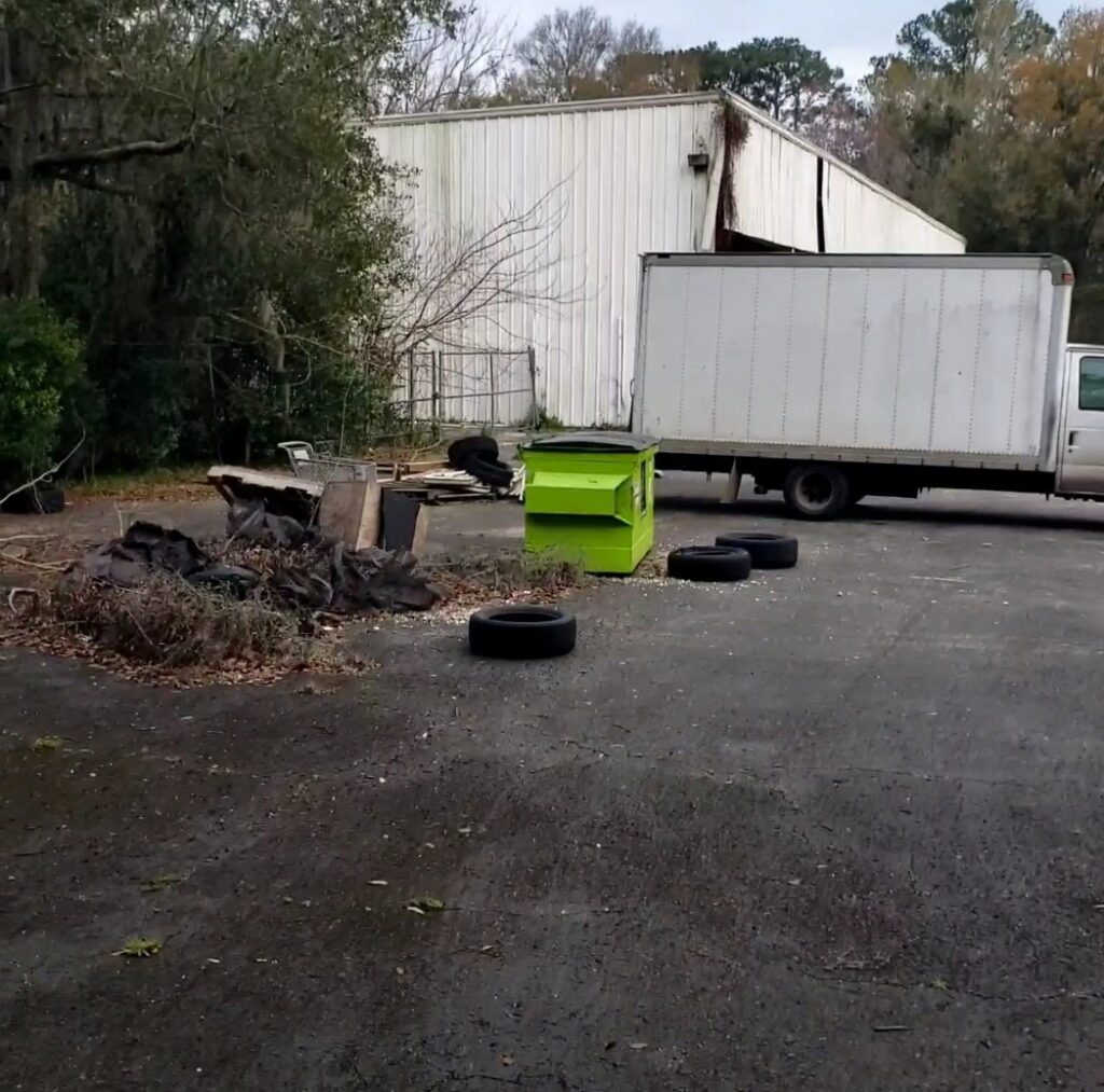 A truck parked next to a pile of debris, old tires, and a green container at a junk removal site by Junk Fade Away, LLC in Jacksonville, FL.