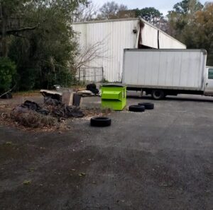 A truck parked next to a pile of debris, old tires, and a green container at a junk removal site by Junk Fade Away, LLC in Jacksonville, FL.