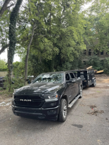 A black RAM truck towing a dump trailer with debris for The Dump Bros LLC on a dirt path in Raleigh, NC.
